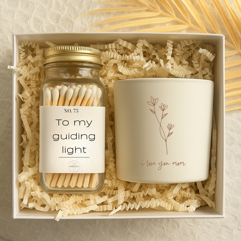 Gift set that includes a candle with a engraved flower design that reads I love you mom and a glass jar with a gold lid that contains white tipped wooden matches. The match jar has a white label that reads to my guiding light. 