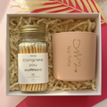 Jar of matches and pink candle with engraved name in a box on a pink and yellow background