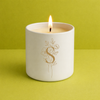 White candle in a jar with a floral design and letter 'S' on a green background