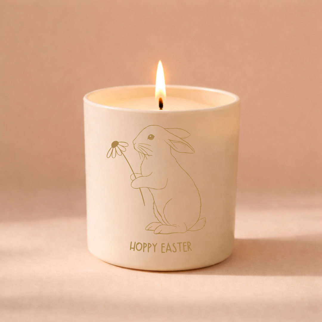 White candle with a engraved bunny holding a flower and below the bunny is text that reads hoppy easter