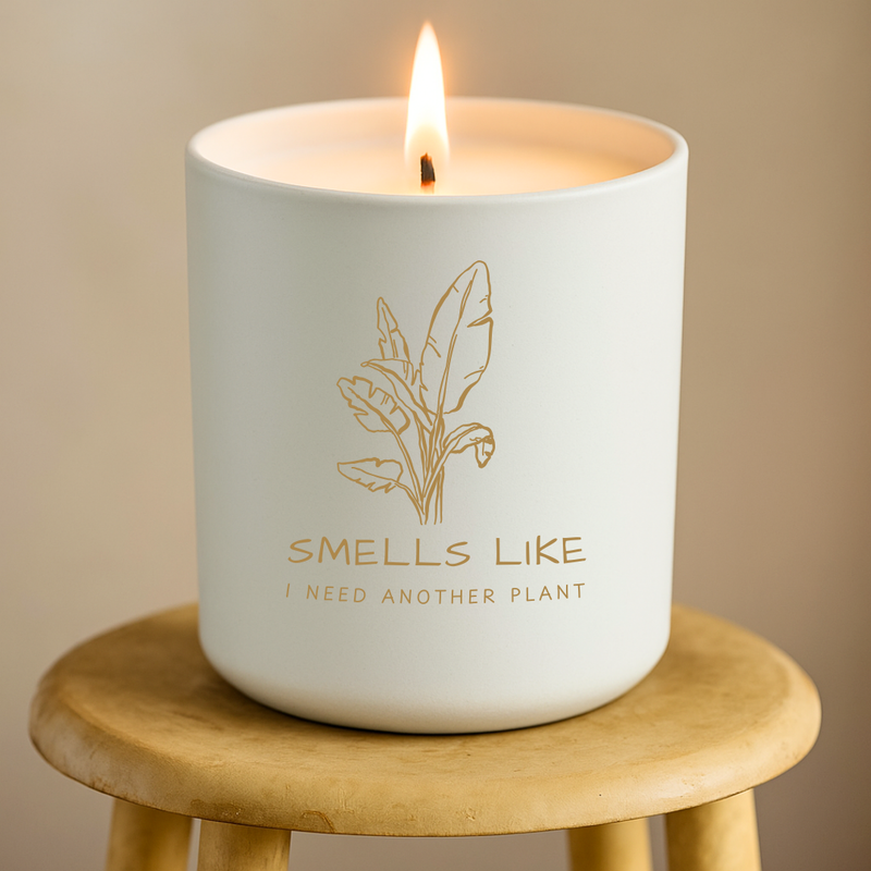 White candle with 'Smells Like I Need Another Plant' text on a beige background