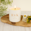 White candle with engraved 'R & K' and a date on a wooden board with flowers and plants.