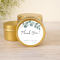Gold tins with 'Thank You!' labels featuring eucalyptus and personalized text on a wooden surface.