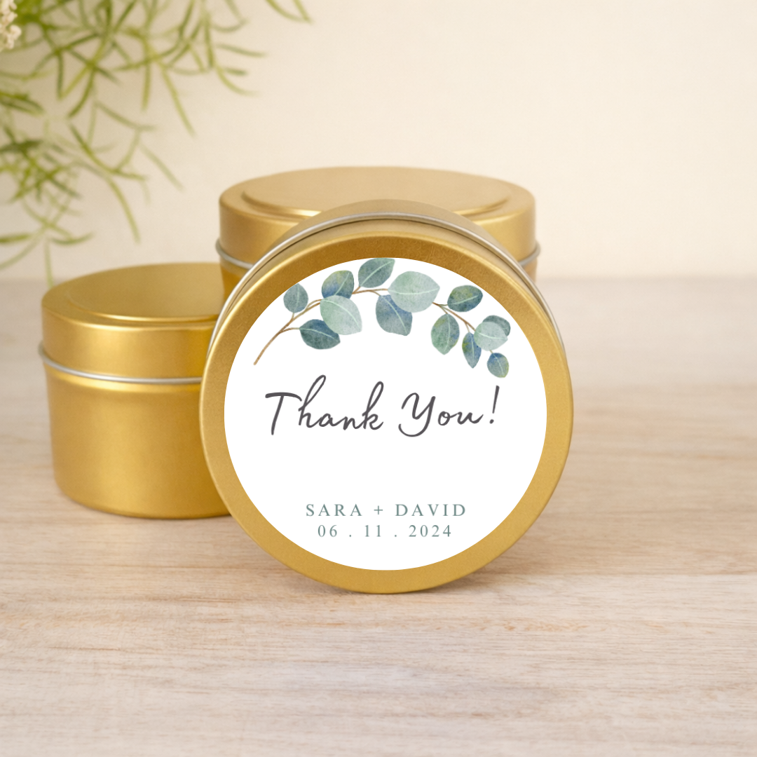 Gold tins with 'Thank You!' labels featuring eucalyptus and personalized text on a wooden surface.