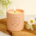 Pink candle with 'Rachel MD' engraving on a wooden surface with flowers.