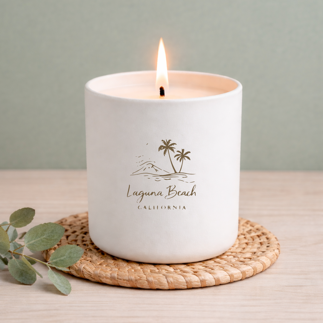 White candle with 'Laguna Beach California' text and palm tree design on a woven coaster.