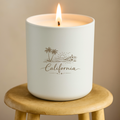 White candle with 'California' design on a wooden stool against a beige background
