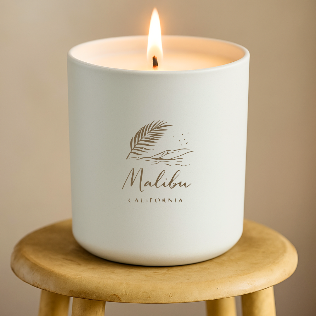 Candle in a white container with 'Malibu California' branding on a wooden stool against a beige background