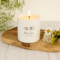 White candle labeled 'Big Sur California' on a wooden board with flowers and greenery.