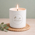 White candle with 'Redondo Beach California' logo on a woven coaster with greenery.