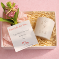 Valentine's Day gift set with a candle, card, and pink flowers in a box on a pink background.